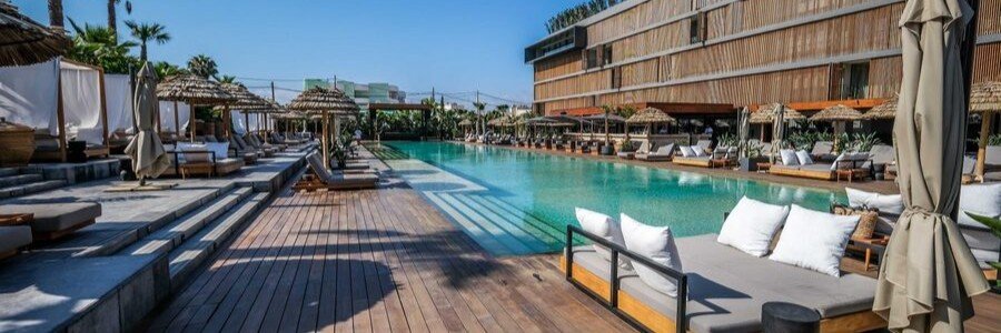 Expansive outdoor swimming pool with wooden decking, luxury daybeds, and thatched umbrellas at OKU Ibiza