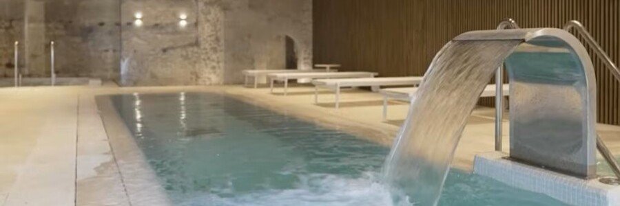 Modern indoor hydrotherapy spa pool with a stainless steel water fountain waterfall at Parador de Ibiza