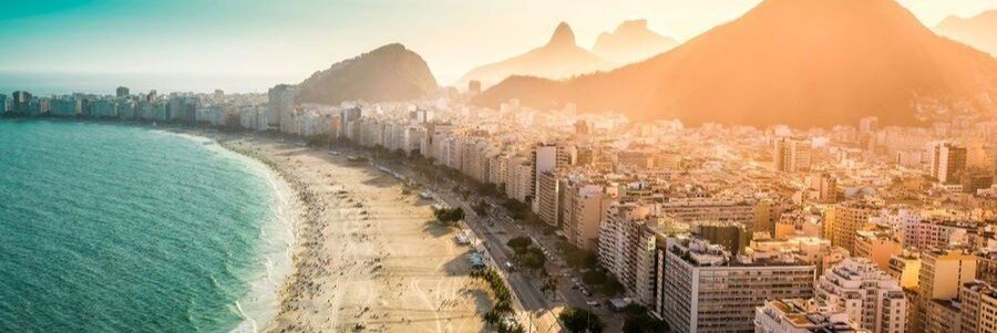 An aerial golden hour view of a sweeping crescent sand strip next to turquoise ocean waters and tall city buildings.