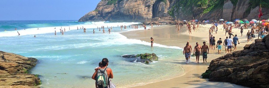 A crowd of people enjoying the sun and turquoise ocean waters at Joatinga Beach next to steep rocky cliffs.