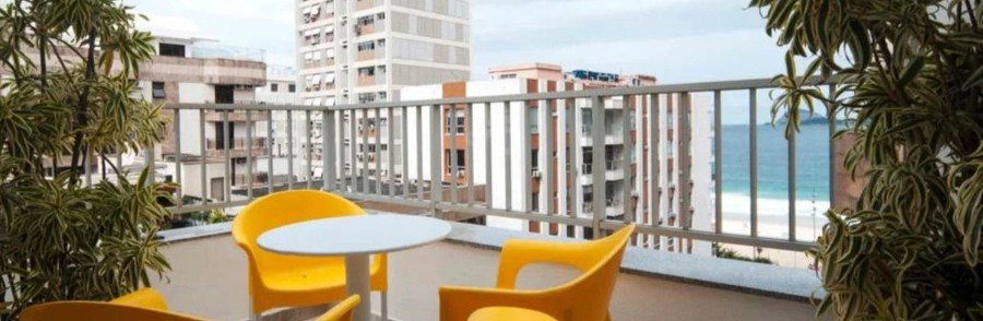 Hotel room balcony with yellow chairs and a round table looking out at Ipanema Beach and city buildings in Rio de Janeiro.
