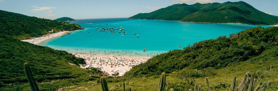 Arraial do Cabo Turquoise Beach and Bay Panoramic view of a white sandy beach, turquoise bay, boats, and green hills at Arraial do Cabo, Brazil.