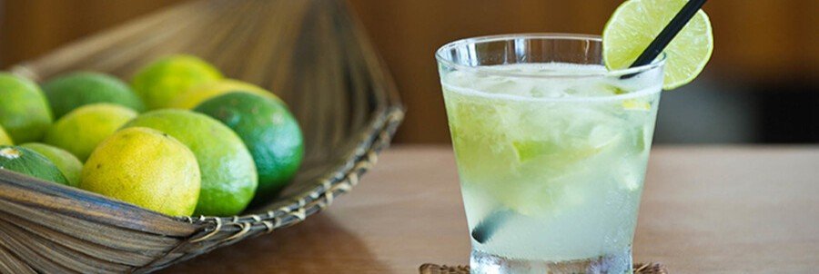 Traditional Brazilian caipirinha cocktail made with fresh lime, sugar, and cachaça served over ice beside whole limes.