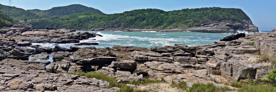 Búzios Beaches and Rugged Atlantic Coastline Layered coastal rocks, blue Atlantic water, and green hills along the rugged shoreline of Búzios, Brazil.
