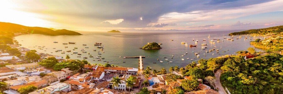 Sunset Over Búzios Harbor and Waterfront Golden sunset over the harbor, anchored boats, coastal islands, and waterfront buildings in Búzios, Brazil.