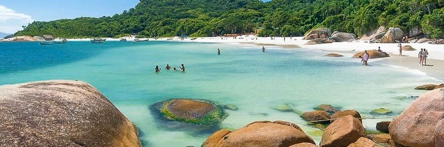 Ilha do Campeche beach in Florianopolis Brazil showing crystal clear turquoise water smooth boulders and white sand coastline