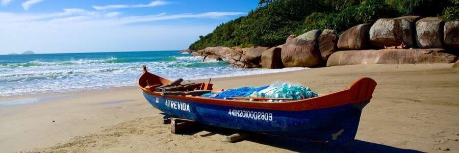 Traditional wooden fishing boat resting on a sandy beach in Florianópolis, Brazil.