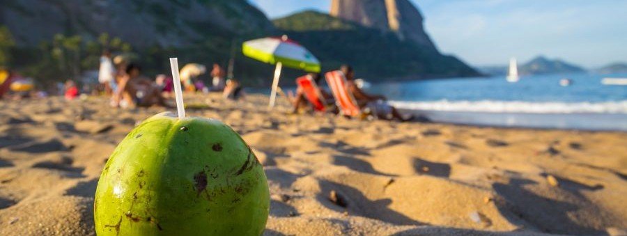 Fresh green coconut with straw on Copacabana Beach sand with beach chairs and ocean in Rio de Janeiro