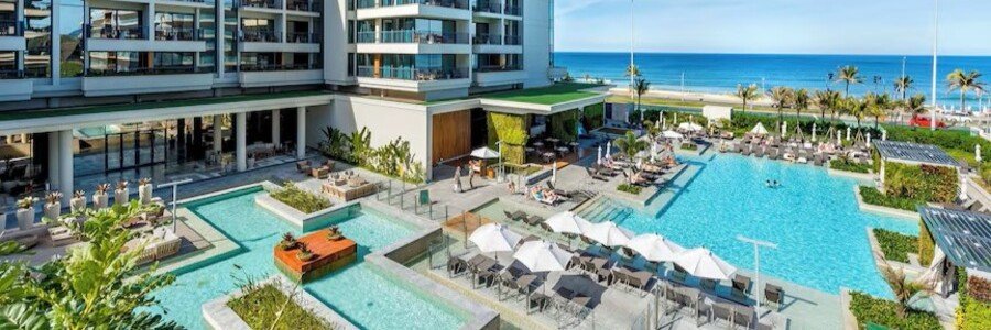 An elevated wide shot of the extensive outdoor pool grounds at the Grand Hyatt Rio de Janeiro, showcasing private cabanas, rows of sun umbrellas, and the blue ocean horizon.