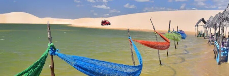 Colorful hammocks suspended over a lagoon in Jericoacoara National Park surrounded by white sand dunes.