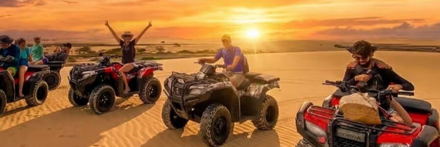 Visitors riding quad bikes across the sand dunes at sunset in Jericoacoara National Park, Brazil.