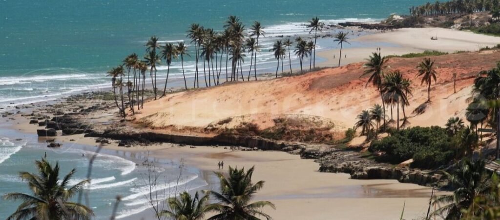 Elevated panorama of Praia da Lagoinha in Ceará Brazil showing curved white sand beach red dunes and coconut palms