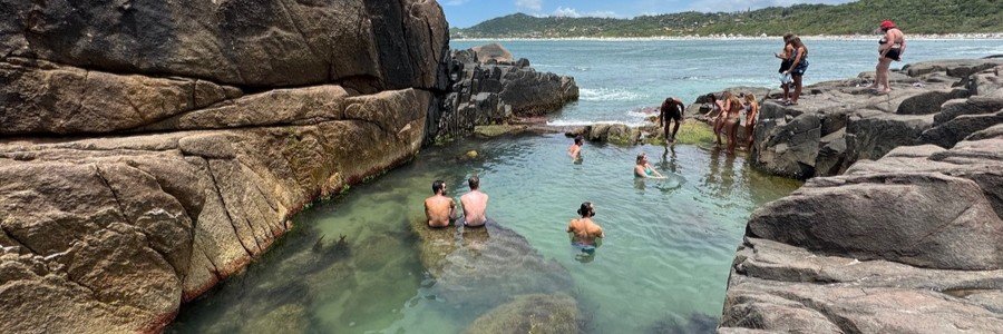 Visitors swimming in natural rock pools along the rugged coastline near Praia do Rosa, Brazil.