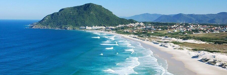 Praia do Santinho Aerial View Florianopolis | Beach Travel Destinations Aerial view of Praia do Santinho with white sand, turquoise water, and rolling green hills.