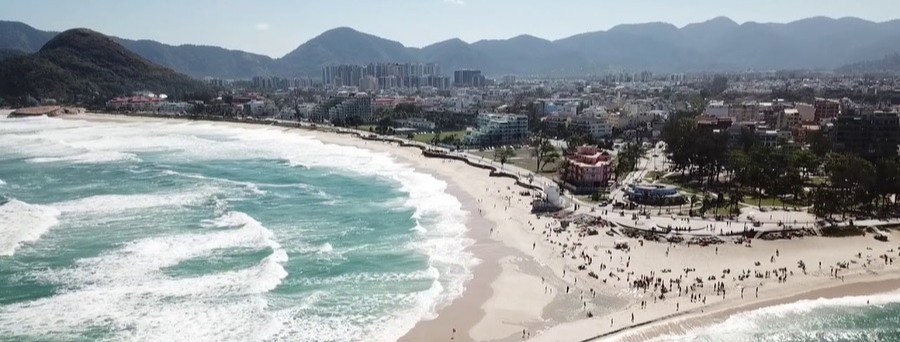 Aerial view of Recreio dos Bandeirantes Beach in Rio de Janeiro with waves rolling onto the wide sandy shoreline and city skyline