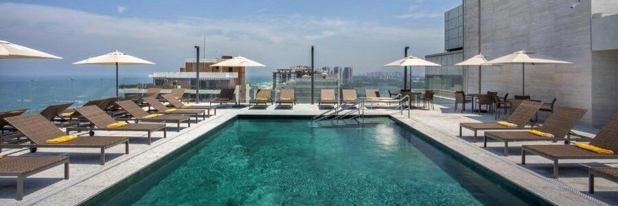 : Rooftop swimming pool deck with wicker lounge chairs and umbrellas at the Windsor Marapendi Hotel in Barra da Tijuca, Rio de Janeiro.