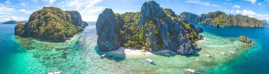 Panoramic aerial view of limestone islands, turquoise water, coral reefs, and white-sand beaches near Boracay and Palawan in the Philippines.