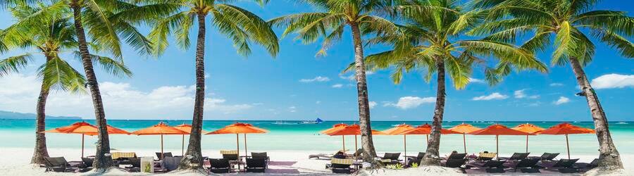Palm trees and orange beach umbrellas lining the white sand shoreline of Boracay’s White Beach.