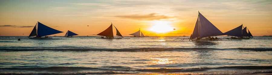 Traditional paraw sailboats drifting across the water during a golden Boracay sunset.