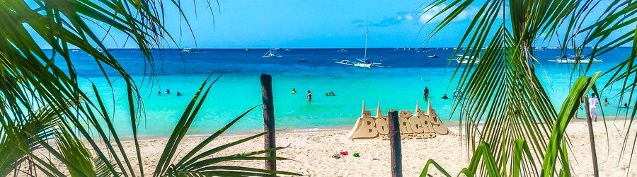 View of turquoise water and sandy shoreline framed by palm leaves at Puka Shell Beach in Boracay.