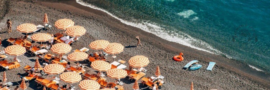 Aerial view of Arienzo Beach near Positano with striped umbrellas, pebble shoreline, and clear blue water along the Amalfi Coast.