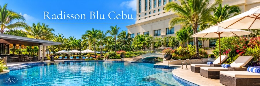 Luxury hotel swimming pool surrounded by tropical palm trees, colorful gardens, elegant lounge chairs, white umbrellas, and a decorative footbridge.