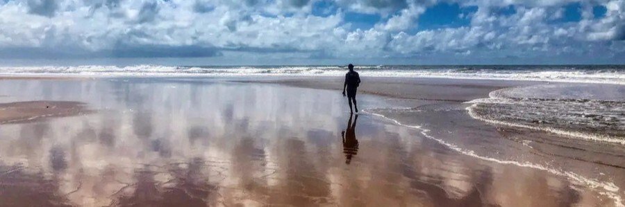 Visitor walking along the reflective shoreline of Taipu de Fora Beach on the Maraú Peninsula in Bahia.