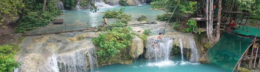 Cambugahay Falls in Siquijor, Philippines, with cascading turquoise waterfalls, lush jungle surroundings, and visitors enjoying the natural pools