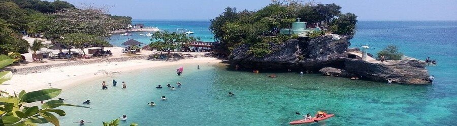 Salagdoong Beach in Siquijor, Philippines, with turquoise water, rocky cliffs, and swimmers enjoying the sheltered cove