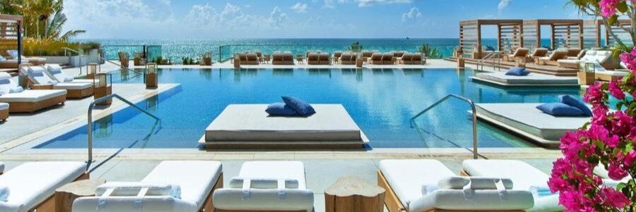 Oceanfront infinity swimming pool at 1 Hotel South Beach with floating daybeds, luxury wooden cabanas, and blooming pink flowers.