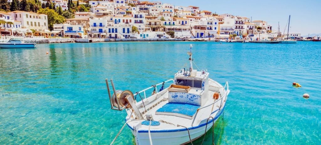Beautiful Andros, Greece—white fishing boat in crystal-clear turquoise harbor with whitewashed houses of Chora on the hillside.