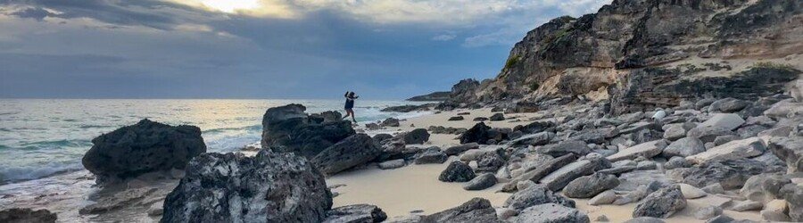 Rocky shoreline in the Bahamas at sunset with waves washing over the rocks.