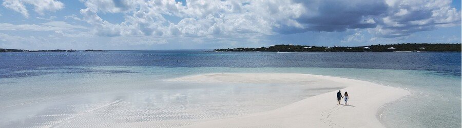 Couple walking across a white-sand tidal flat in the Abacos on a calm, clear day.