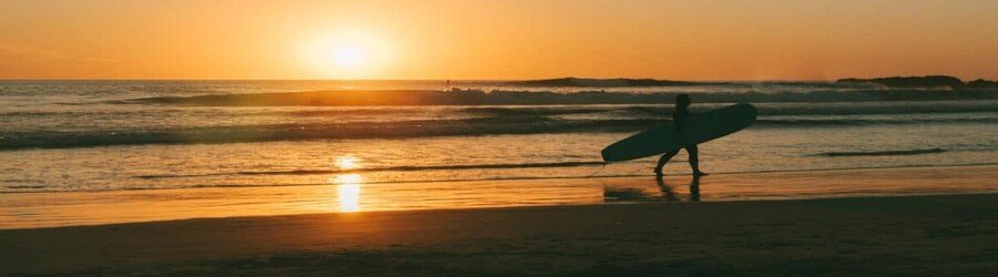 Silhouette of a surfer walking along the shoreline at sunset with waves breaking in the Sea of Cortez.