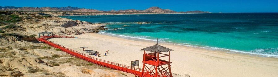 Red wooden boardwalk leading to a wide white sand beach with bright turquoise water in the Sea of Cortez.