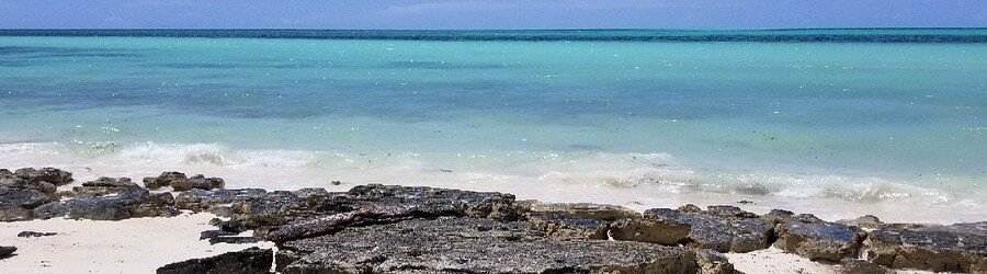 Clear turquoise water and light sand with rocky shoreline at Fortune Beach in Grand Bahama.