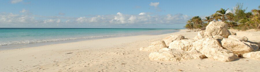 Quiet white sandy beach on Grand Bahama with smooth rocks and calm turquoise water.