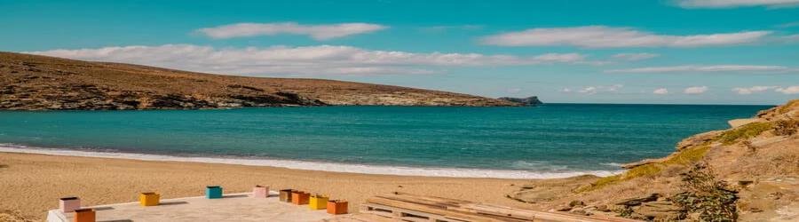 Wide sandy stretch of Kolympithra Beach in Tinos with gentle waves and rocky landscape.