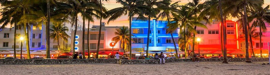 Colorful Art Deco buildings on Ocean Drive lit up at sunset with palm trees lining the beach.