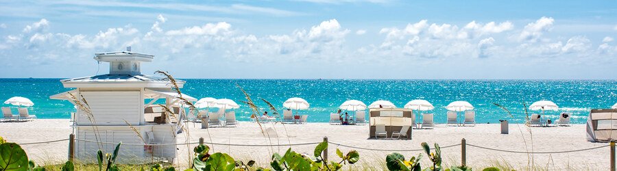 Bright blue water and white umbrellas along the beachfront on 64th Street in Miami Beach.