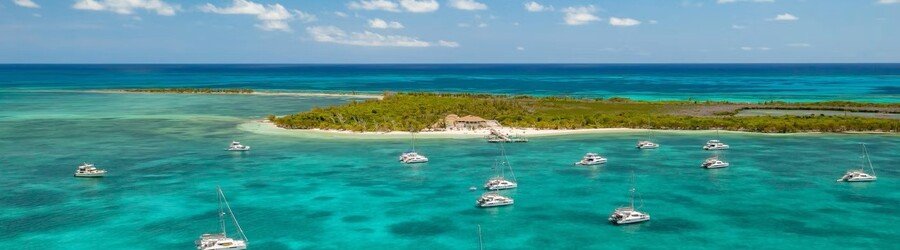 Dozens of sailboats anchored in clear turquoise waters near a small cay in the Abacos.