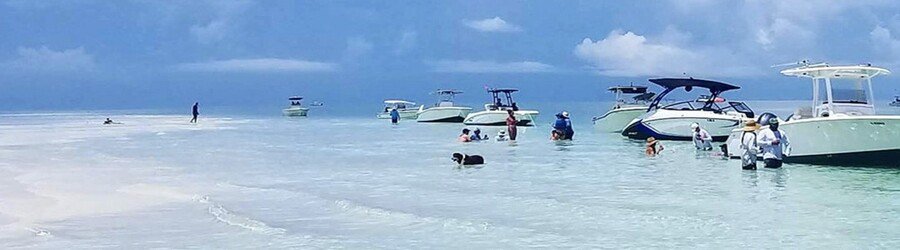 People wading in shallow water near anchored boats at the Islamorada Sandbar
