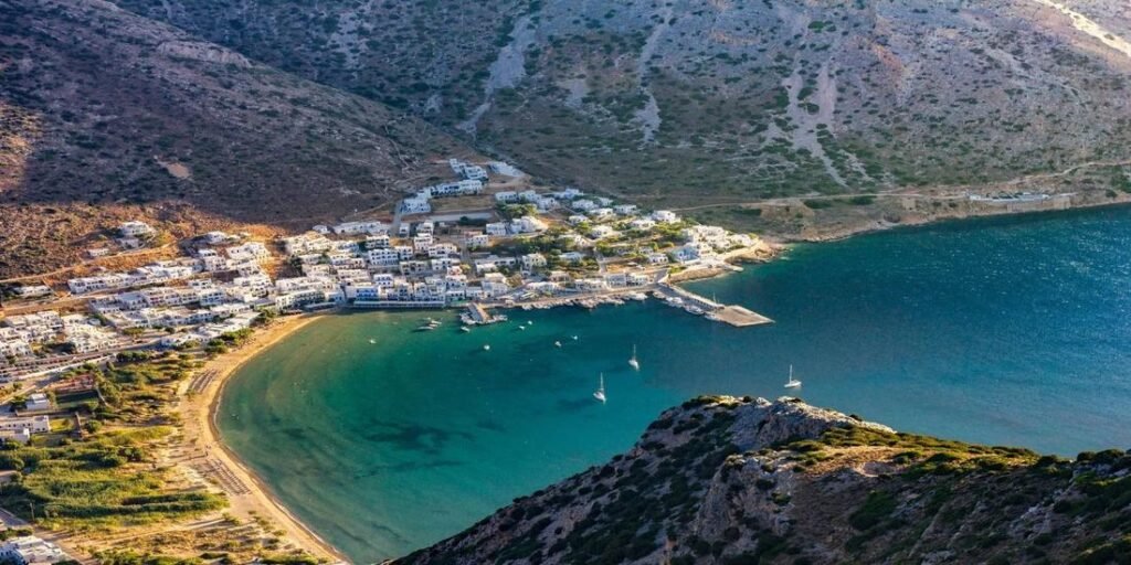 Aerial view of Kamares Bay in Sifnos, Greece, with whitewashed houses, sandy beach, and turquoise sea surrounded by rocky hills.