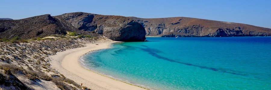 Curved turquoise beach in Todos Santos Mexico with golden sand, rocky desert cliffs, and clear blue water under a sunny sky