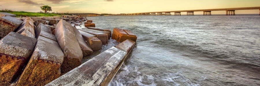 Scenic waterfront view near Amelia Island featuring coastal rocks, ocean waters, and a bridge at sunset.