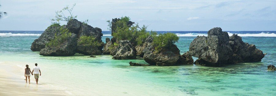 Couple walking along a beach in the Austral Islands with turquoise water and large rock formations