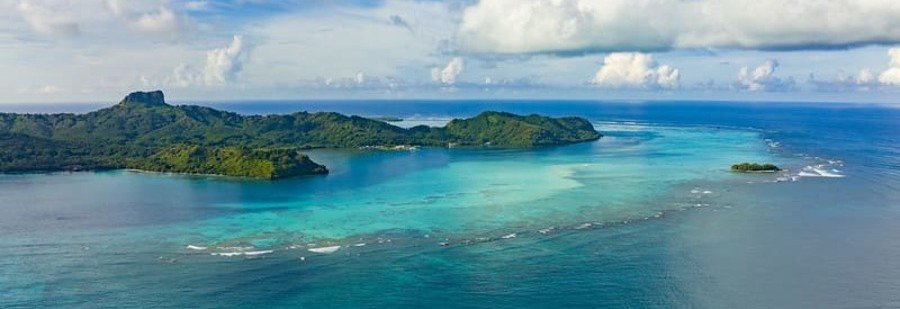 Aerial view of the Austral Islands with turquoise lagoon, coral reefs, and lush green volcanic hills in French Polynesia