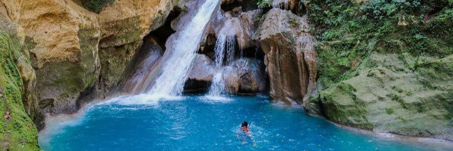 Waterfall flowing into a vivid blue swimming pool surrounded by rocks and tropical forest at Bassin Bleu near Jacmel, Haiti.