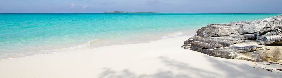 White sand beach in the Berry Islands with turquoise water and a rocky shoreline under a bright, clear sky.