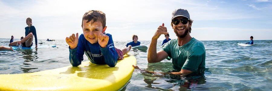 Family surf lesson in Boca Raton Florida with instructor and child on surfboard in shallow Atlantic water